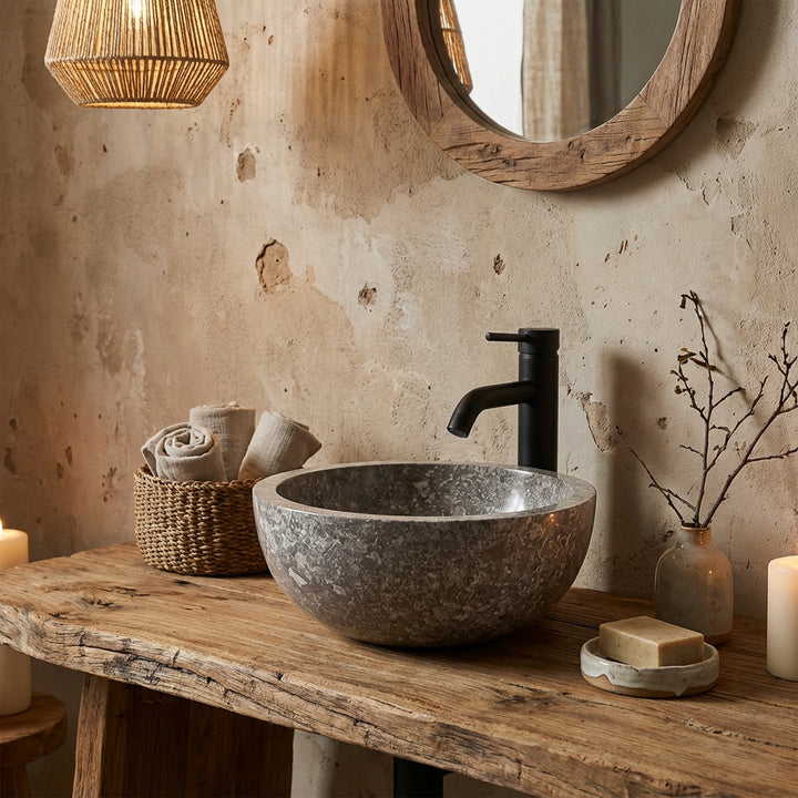 Vasque à poser ronde en pierre sur plan en bois rustique avec robinetterie noire dans une ambiance de salle de bain naturelle