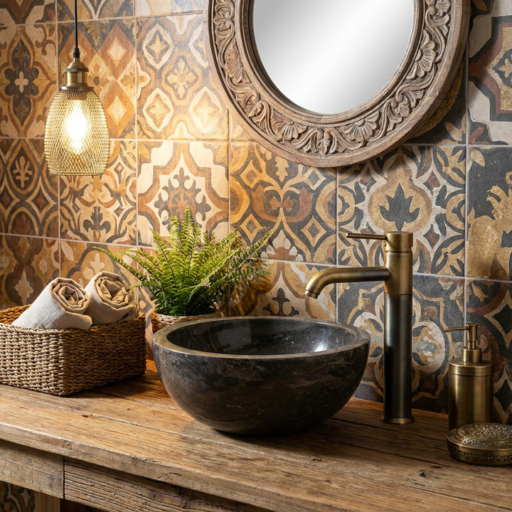 Vasque ronde à poser en pierre sur vasque en bois avec robinetterie en laiton devant carrelage à motifs dans une ambiance salle de bain chaleureuse