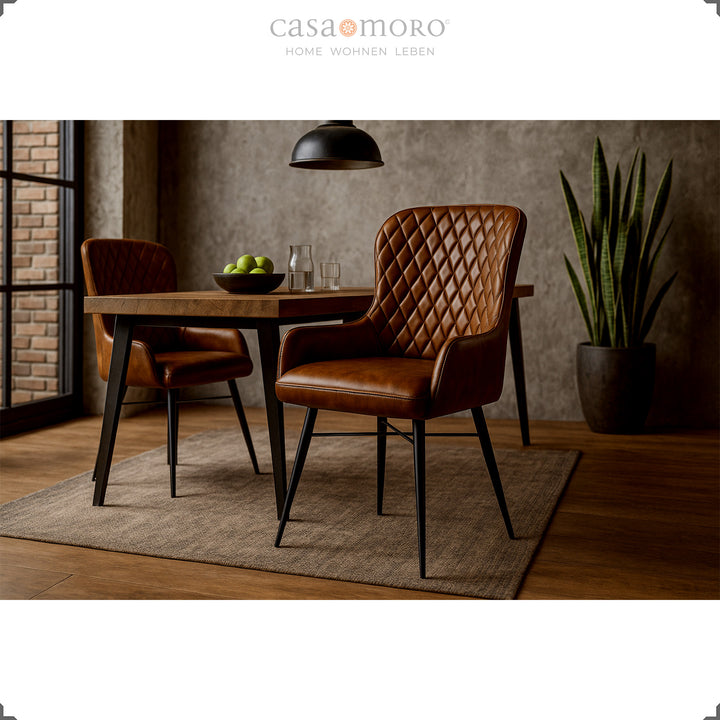 Two antique brown leather chairs with diamond quilting at a wooden table in the modern dining room with a concrete wall, wooden floor and green houseplant.