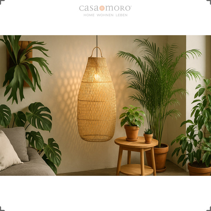 Grande lampe suspendue en rotin dans le salon avec beaucoup de plantes vertes et une lumière douce