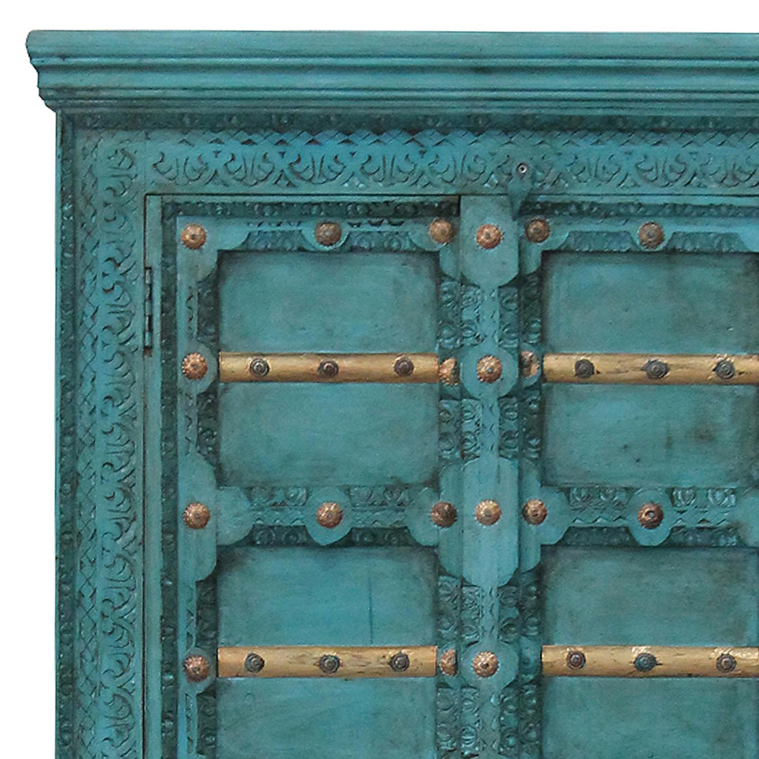 Detail der türkisfarbenen Schrankfront mit geschnitzten Ornamenten, goldfarbenen Leisten und Beschlägen.