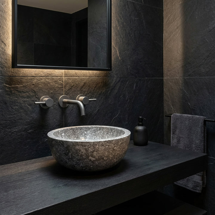 Rond Lavabo en pierre naturelle foncée comme fixation sur une console noire dans une ambiance de salle de bain moderne et minimaliste