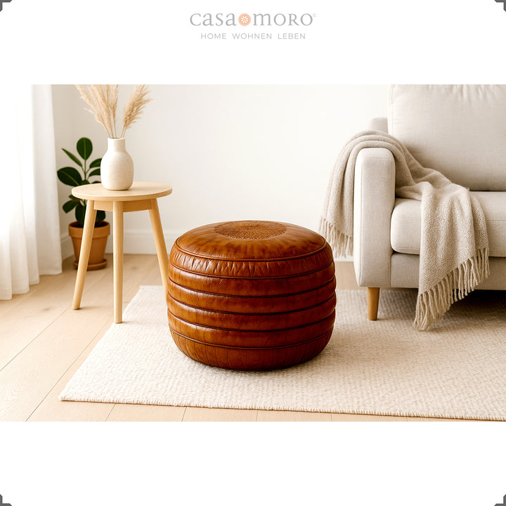 Bright Scandinavian-style living room with a round leather pouf in brown on a carpet, a beige sofa and a wooden stool with a vase - a calm, natural ambience.