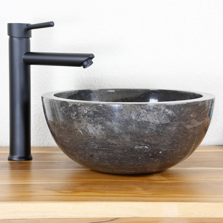 Lavabo rond en pierre en matériau naturel foncé comme fixation sur un plan en bois avec un raccord noir, décor de studio épuré