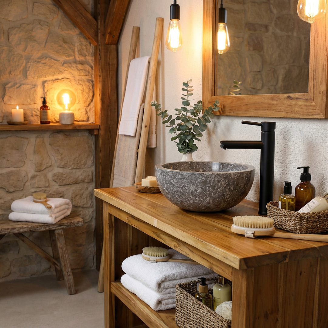 Vasque ronde à poser en pierre sur une console en bois massif avec raccords noirs dans un style de salle de bain chaleureux et rustique