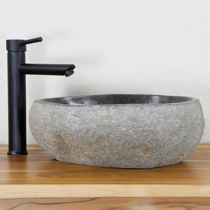 Lavabo Fabriqué en pierre naturelle grise de forme ovale, associé à des ferrures noires sur un plateau en bois chaleureux
