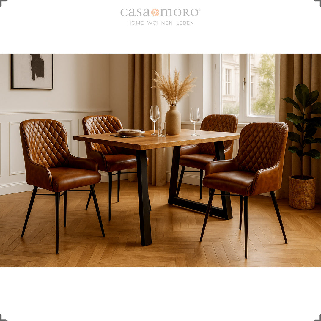 Four antique brown leather chairs with diamond quilting at a wooden table in an elegant dining room with parquet floors, light wall paneling and natural decorations.