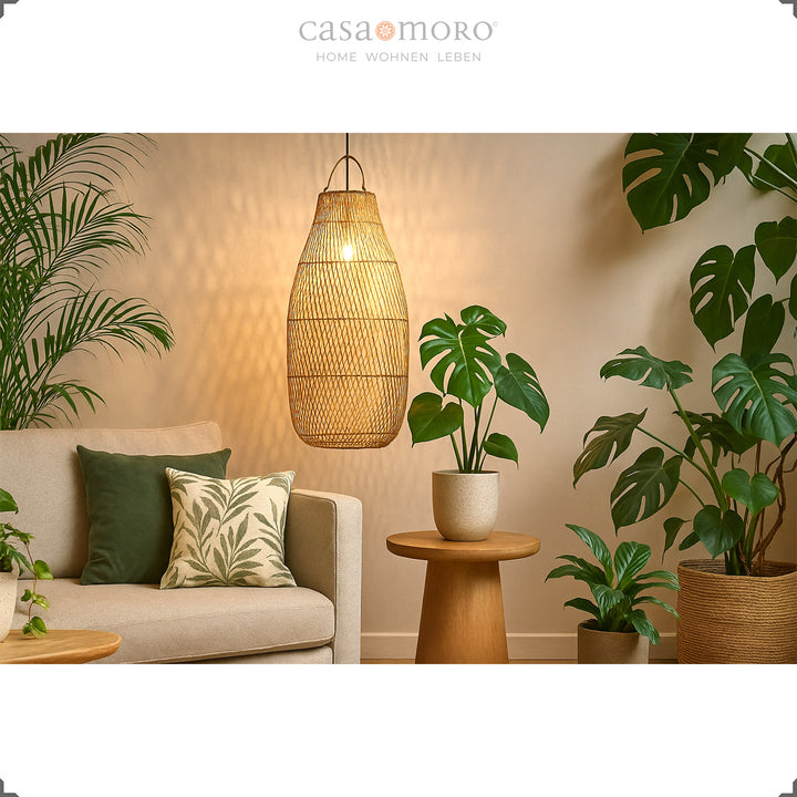 Grand plafonnier en rotin au-dessus du canapé dans le salon avec beaucoup de plantes vertes et une lumière chaude
