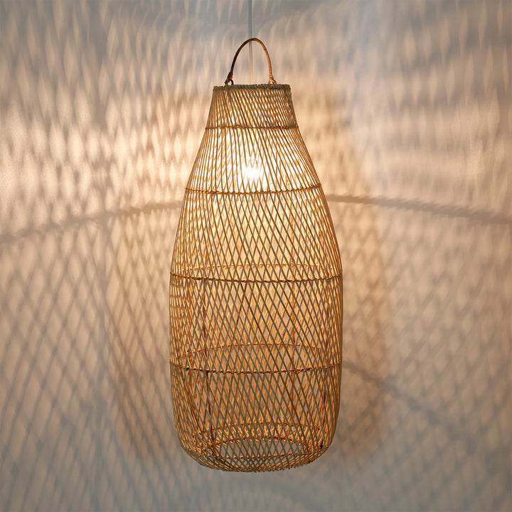 Lampe haute en rotin au motif de tissage fin et jeu de lumière chaleureux sur le mur