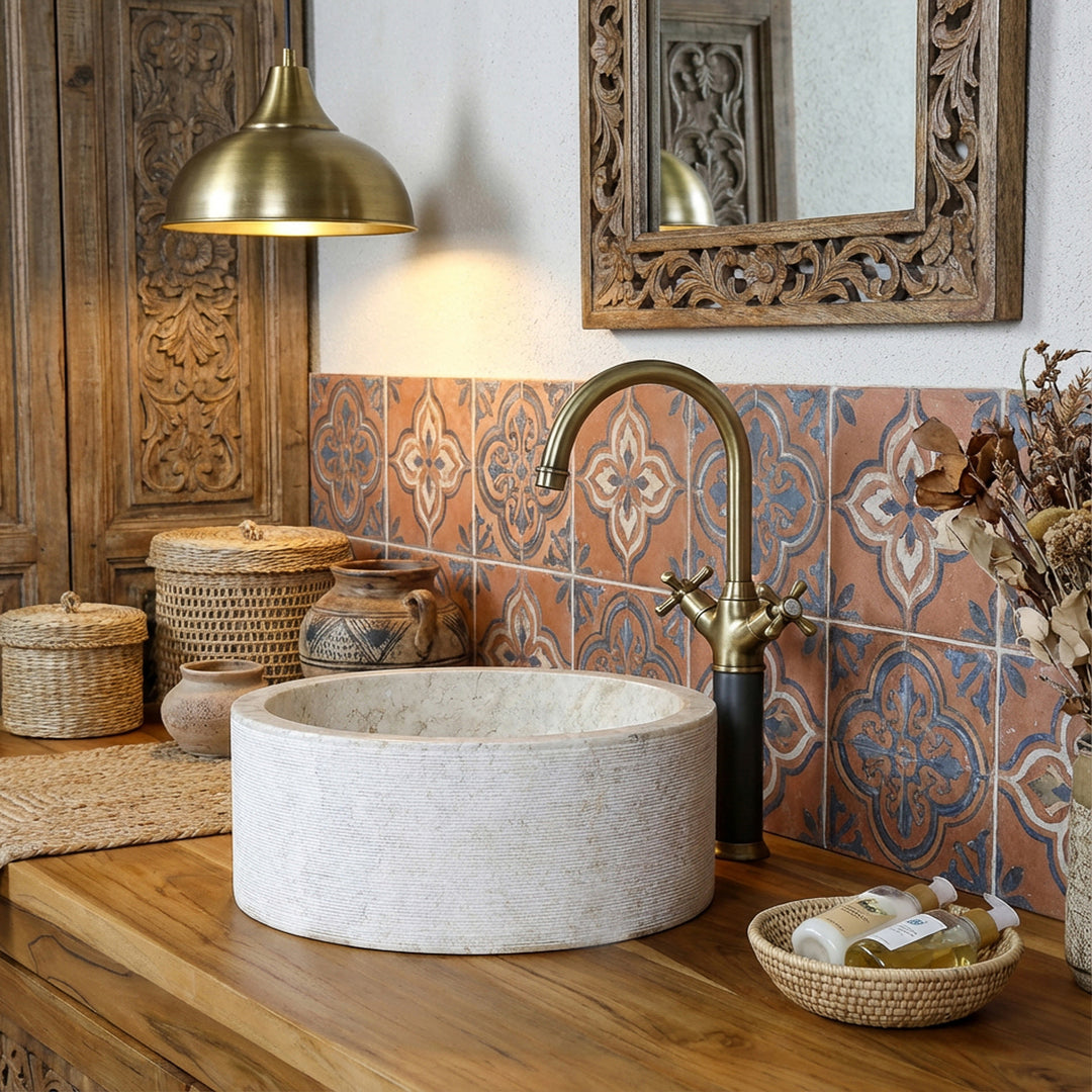Round stone washbasin in a warm marble look on a wooden console, complemented by brass fittings and oriental tiles.