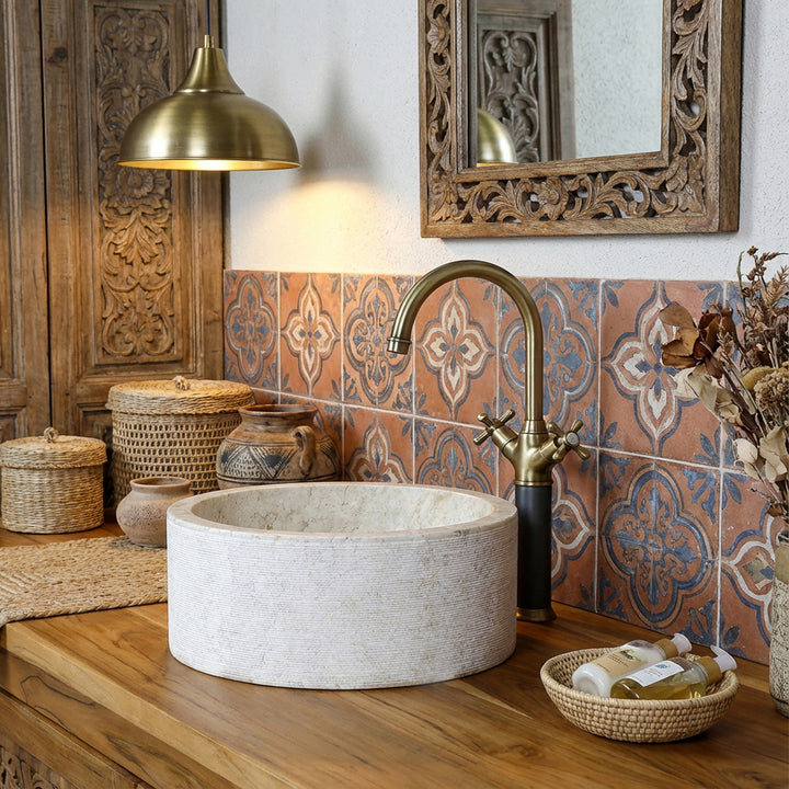 Round stone washbasin in a warm marble look on a wooden console, complemented by brass fittings and oriental tiles.