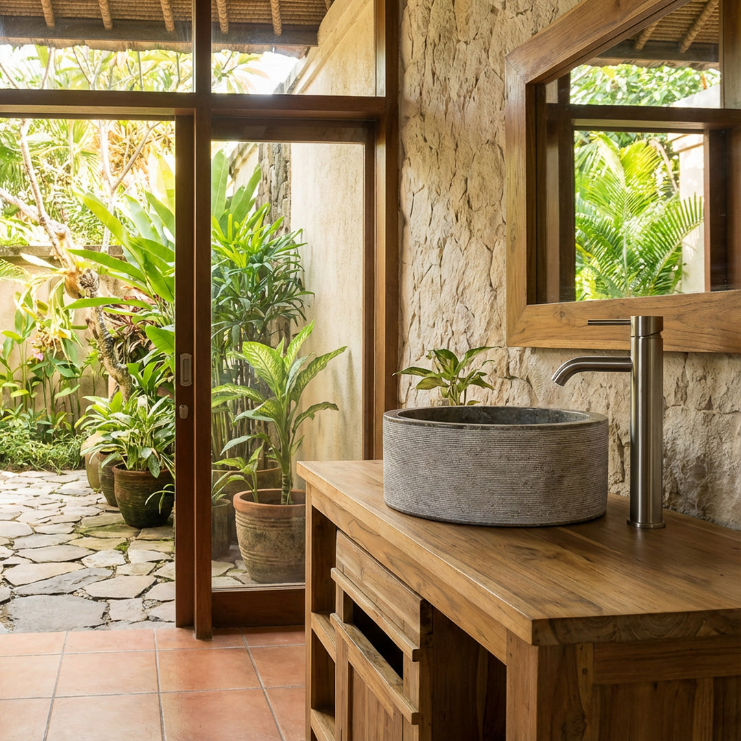 Lavabo rond en pierre grise sur meuble sous vasque en bois, placé dans la salle de bain baignée de lumière avec vue sur le jardin.