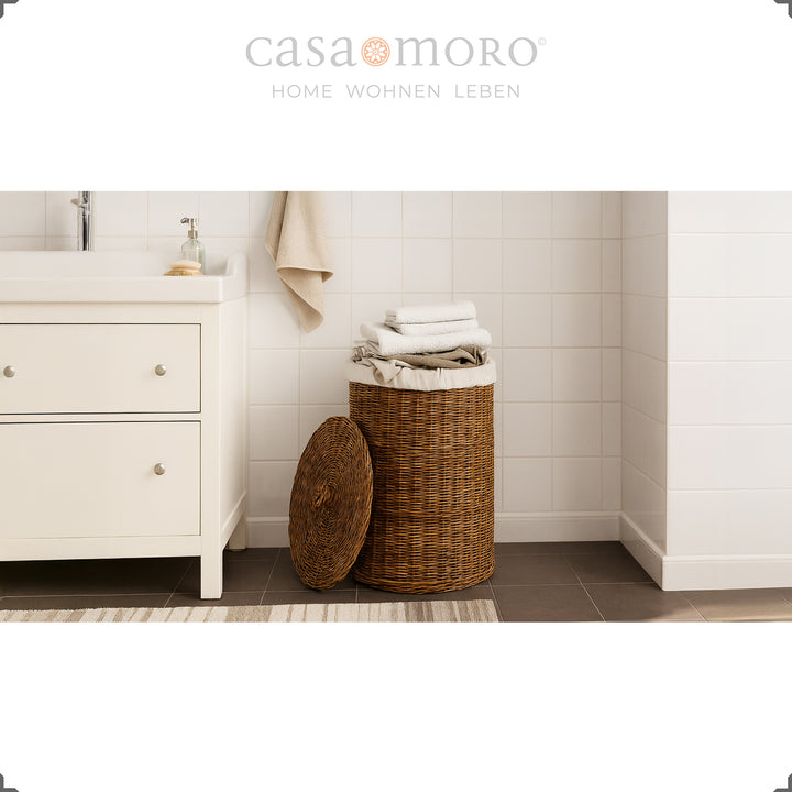 Panier à linge en rotin marron avec couvercle et insert en coton dans la salle de bain, rempli de serviettes de manière décorative