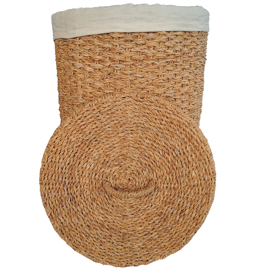 Wäschekorb aus naturfarbenem Seegras mit hellem Stoffeinsatz und davor aufgestelltem Deckel.